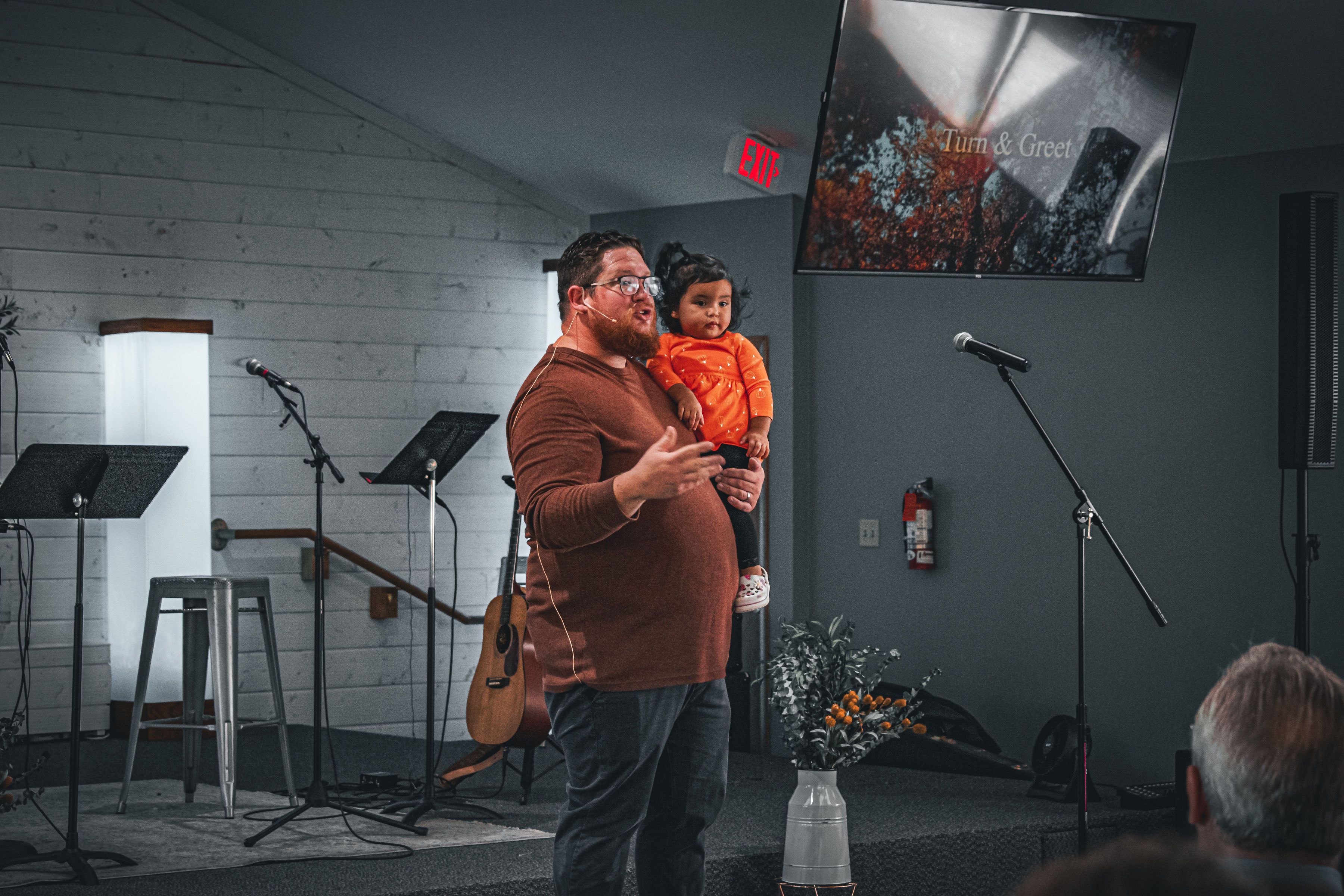 Pastor Mark speaking while holding a young child